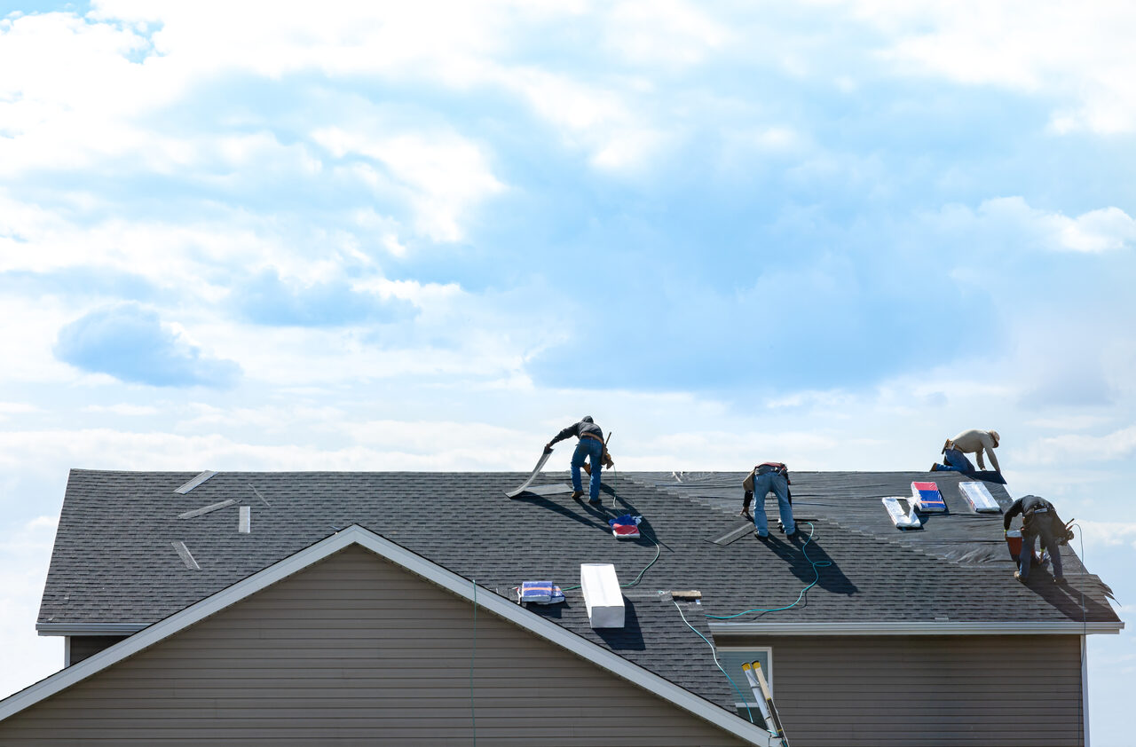A roofing crew working across a pitched shingle roof