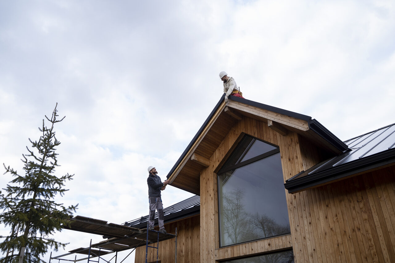 A roofing crew installing metal panels with scaffolding on a residential roof
