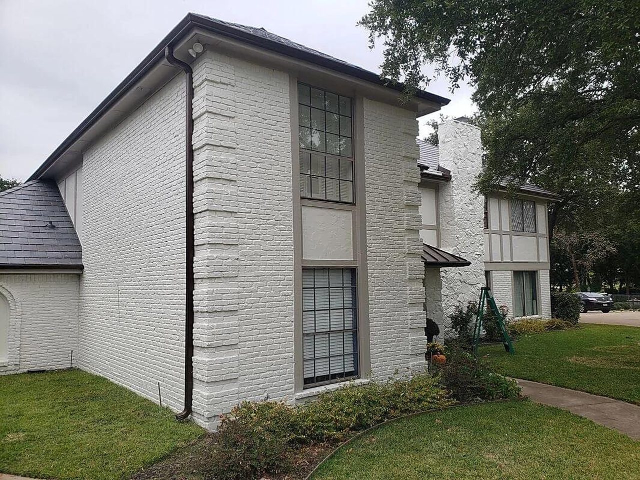 A painted brick two story house with dark seamless gutters and a downspout