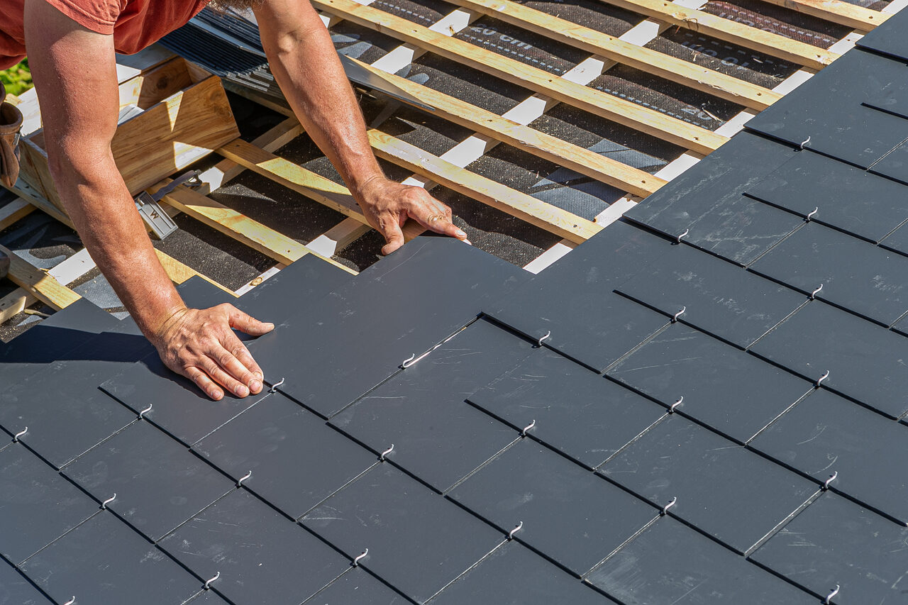 A roofer hand laying shingles across a new roof deck