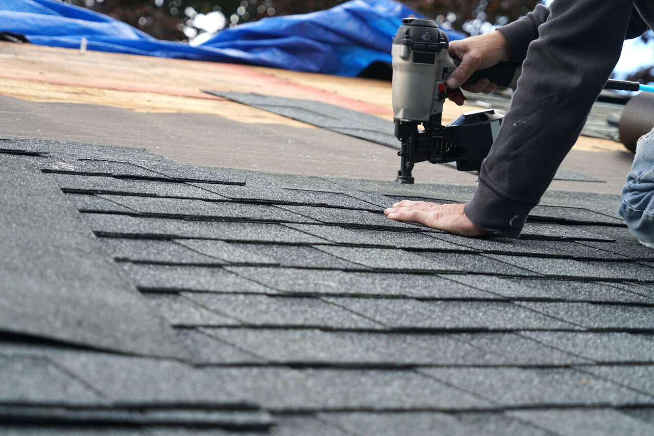 A nail gun being used to fasten architectural shingles on a roof deck