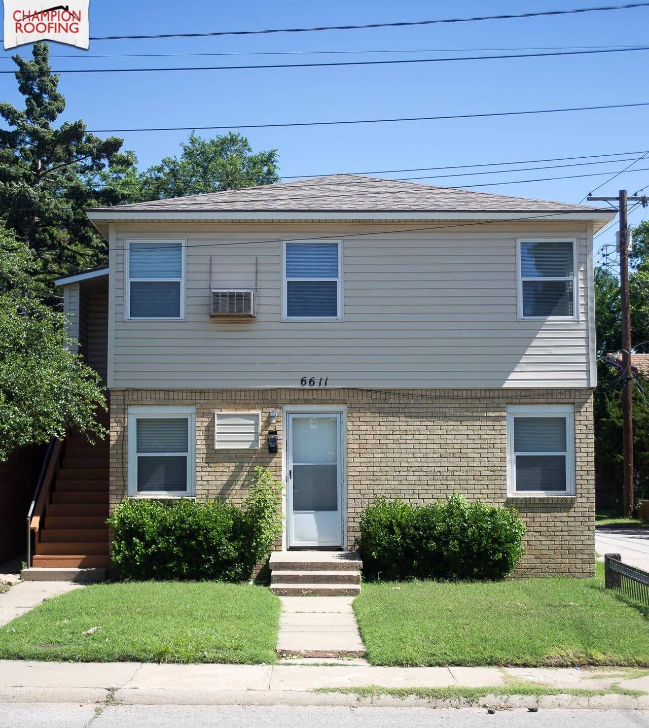 A two storey multifamily building with a Champion Roofing yard sign in front