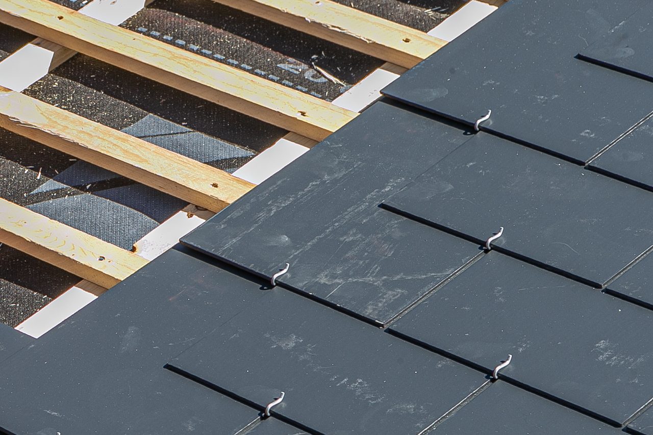 Dark slate style tiles hooked over wooden battens, with the underlayment showing between the battens