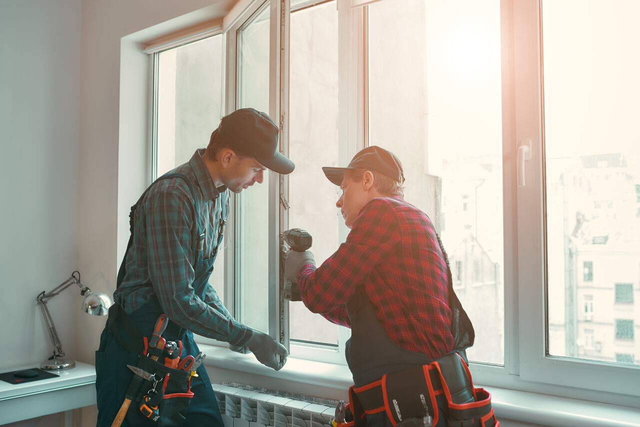 Two installers fitting a window frame from inside the room